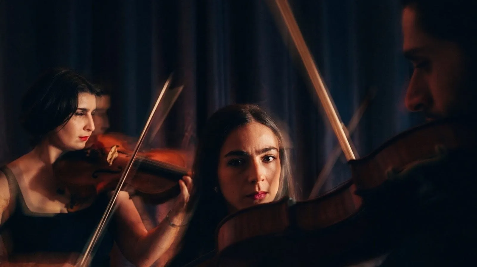 Tres músicos de cuerdas tocan bajo una luz cálida